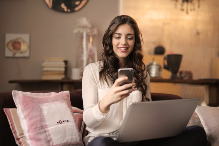 woman-sitting-on-sofa-while-looking-at-phone-with-laptop-on-920382 (1)